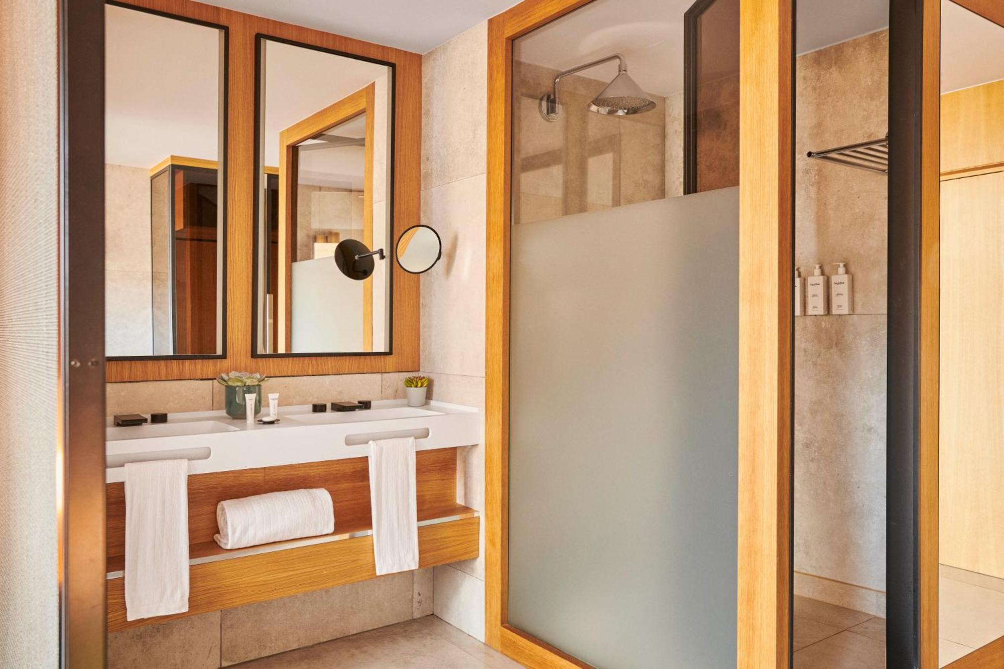 ホテル ソフィア バルセロナ イン ザ アンバウンド コレクション バイ ハイアット エクステリア 写真 The photo depicts a modern bathroom featuring a combination of natural materials and sleek design. There are three mirrors mounted on the wall above a wooden vanity. The vanity includes a basin and is adorned with toiletries and a small plant. On the