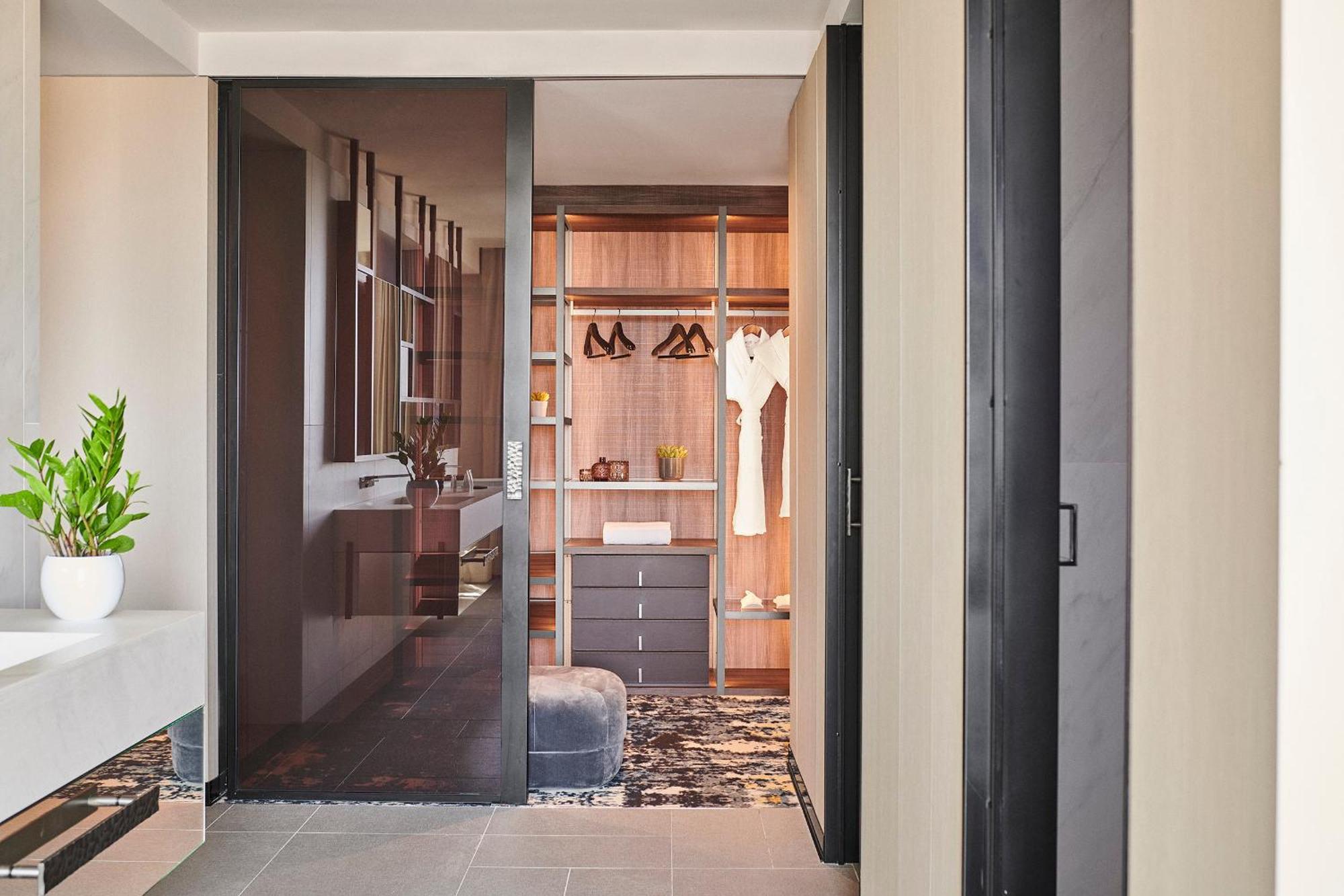 ホテル ソフィア バルセロナ イン ザ アンバウンド コレクション バイ ハイアット エクステリア 写真 The photo shows a modern and stylish interior space, likely a bedroom or a dressing area. In the foreground, there is a glass door leading into a closet. The closet has a wooden interior with hanging clothes, including several garments on hangers. Th